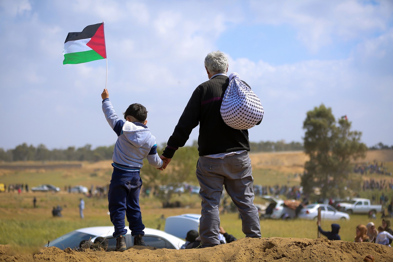 A Palestinian grandfather holding the hand of his grandson who is raising the Palestinian flag in peace finally. In a grassy field under the sun